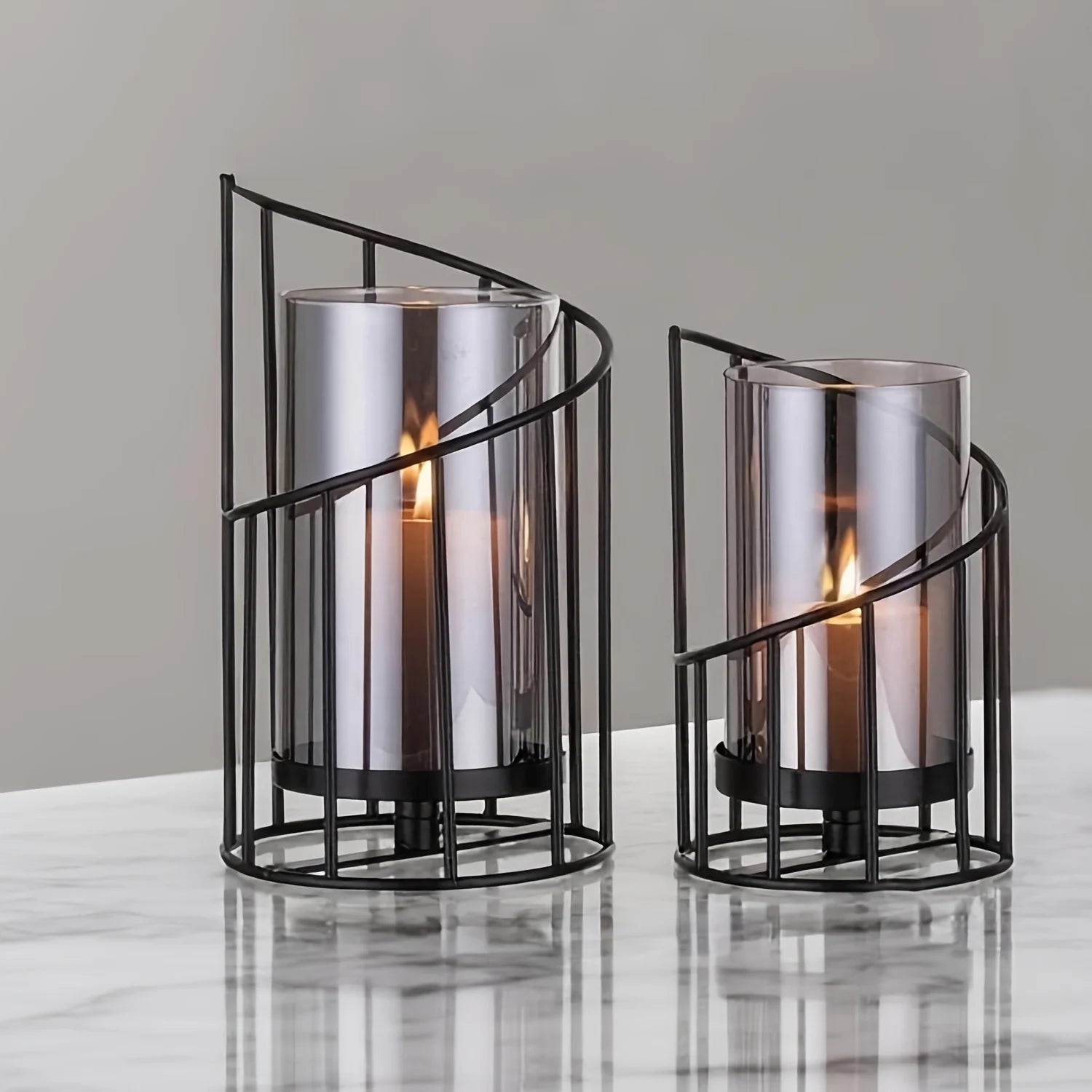 Set of two modern black spiral glass candle holders with smoked hurricane glass displayed on a wooden table in a contemporary home interior.