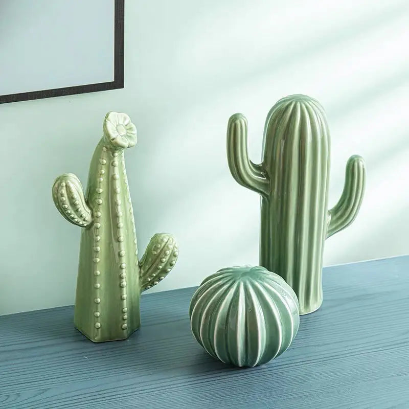 Three ceramic cactus sculptures on a wooden surface with a light blue wall in the background.