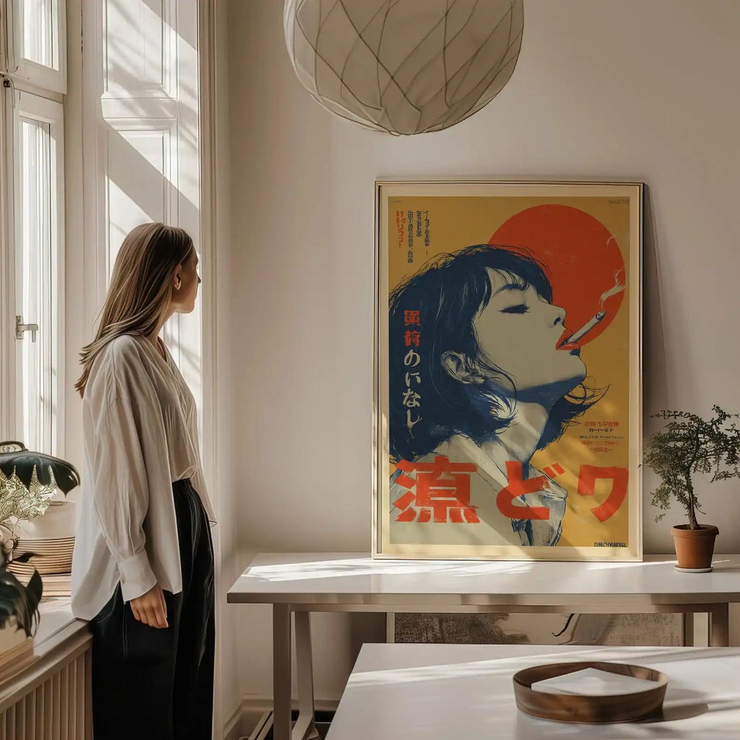A woman stands by a window in a sunlit room, looking at a framed vintage-style poster hanging on the wall above a table. The poster features a stylized portrait with a large red sun and bold red and black text on a yellow background.