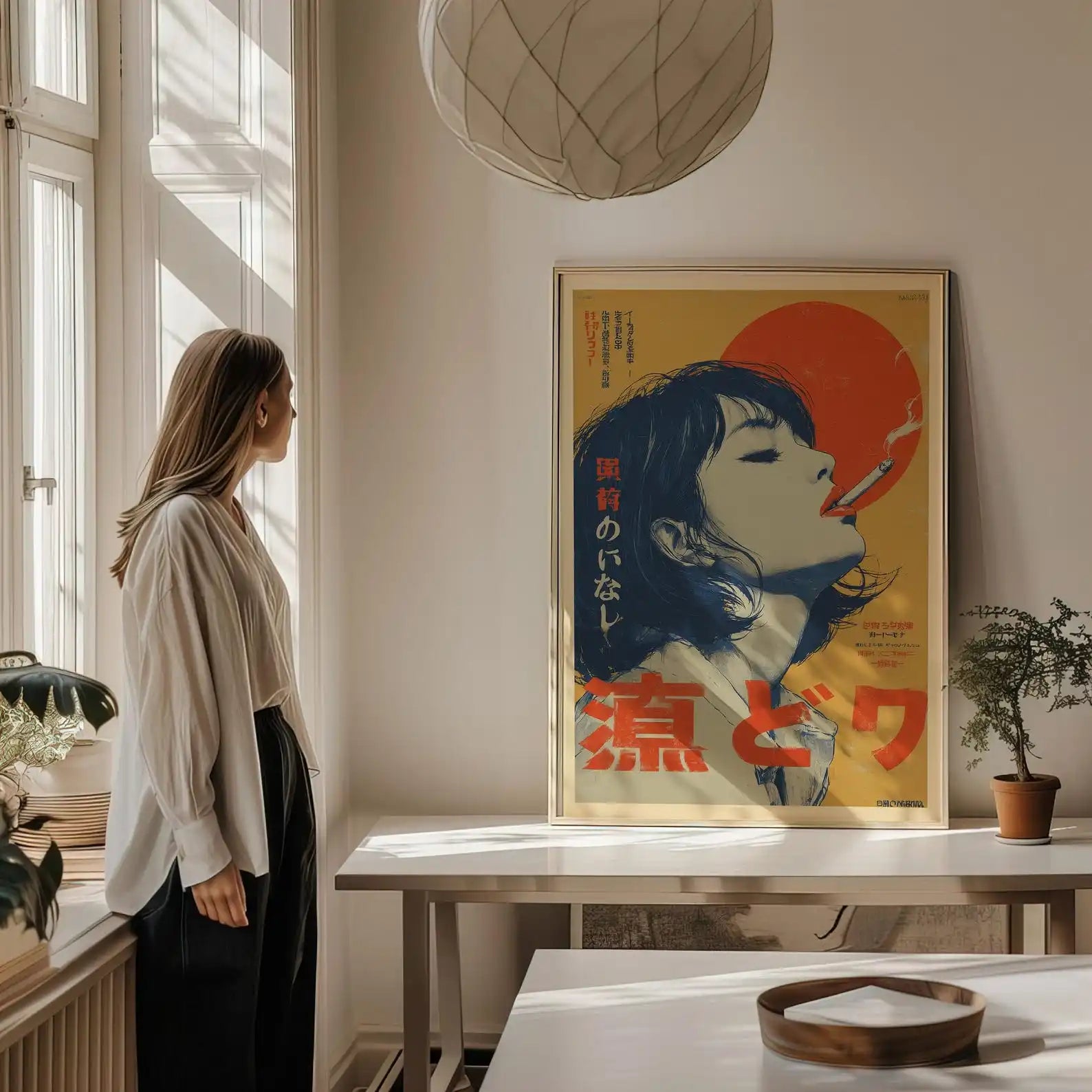 A woman stands by a window in a sunlit room, looking at a framed vintage-style poster hanging on the wall above a table. The poster features a stylized portrait with a large red sun and bold red and black text on a yellow background.