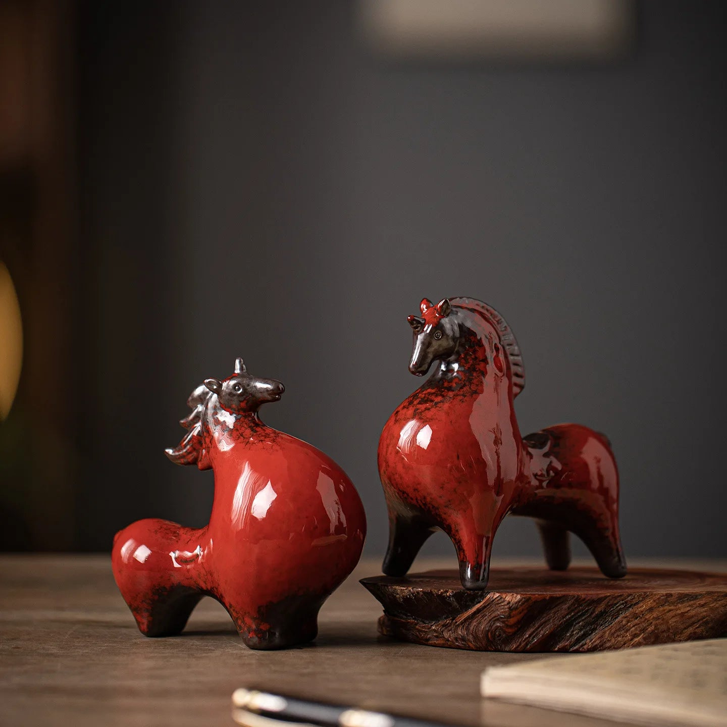 Two red ceramic horse figurines on a wooden surface with a dark background