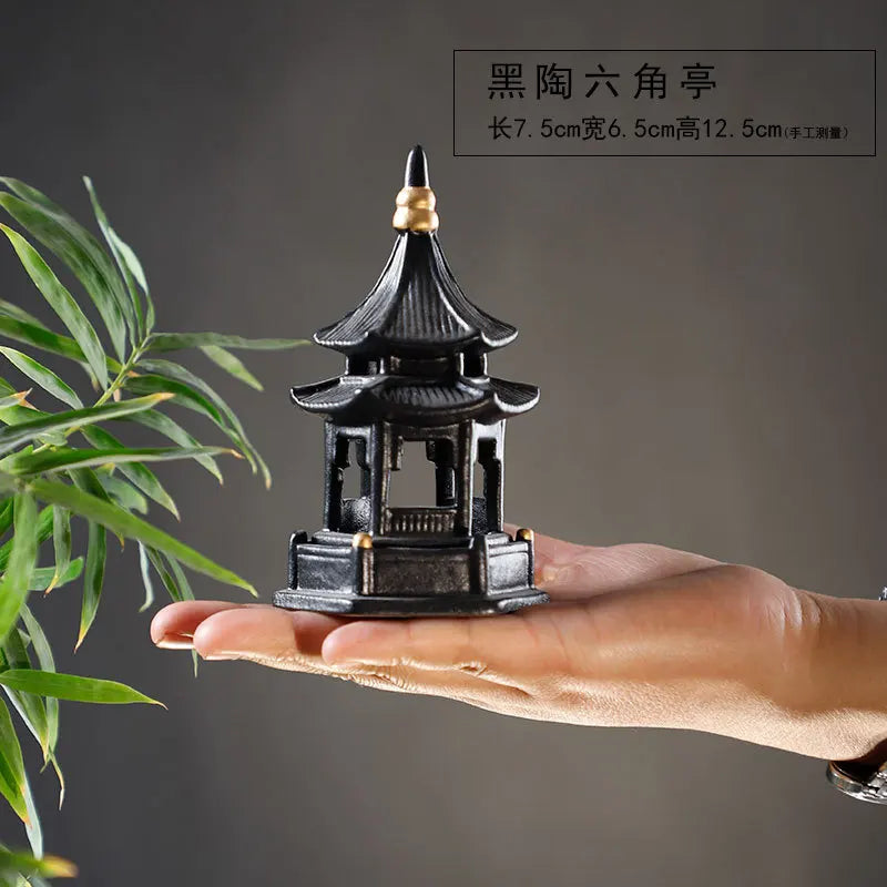 Small black pagoda model held in a hand with a plant on a dark background