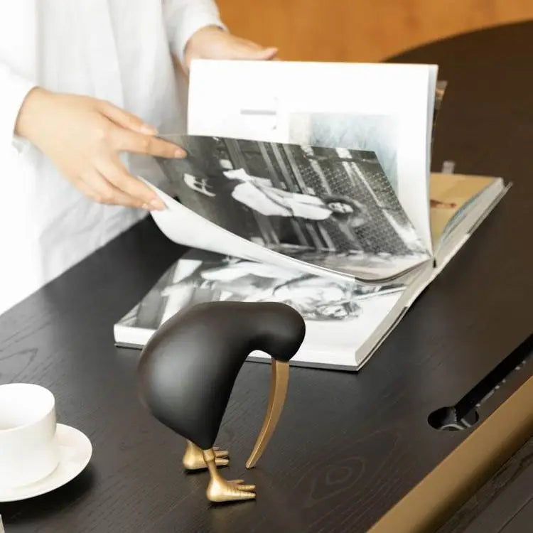 Person flipping through a photo album on a desk with a decorative modern bird figurine in the foreground.