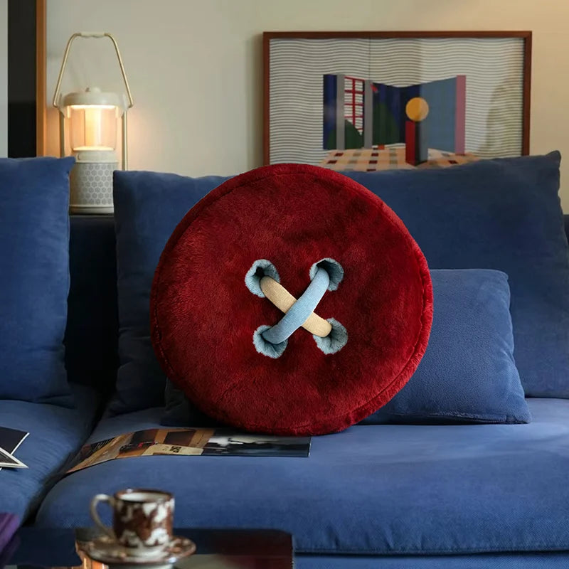 Red button-shaped pillow on a blue sofa with a lamp and artwork in the background