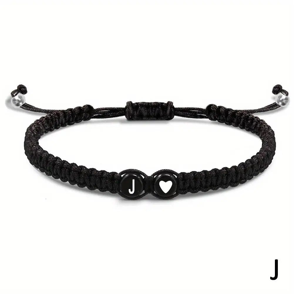 Black braided bracelet with a heart and letter 'J' charm on a white background