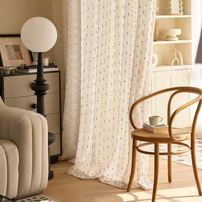 Living room with beige armchair, wooden chair, and patterned curtains.