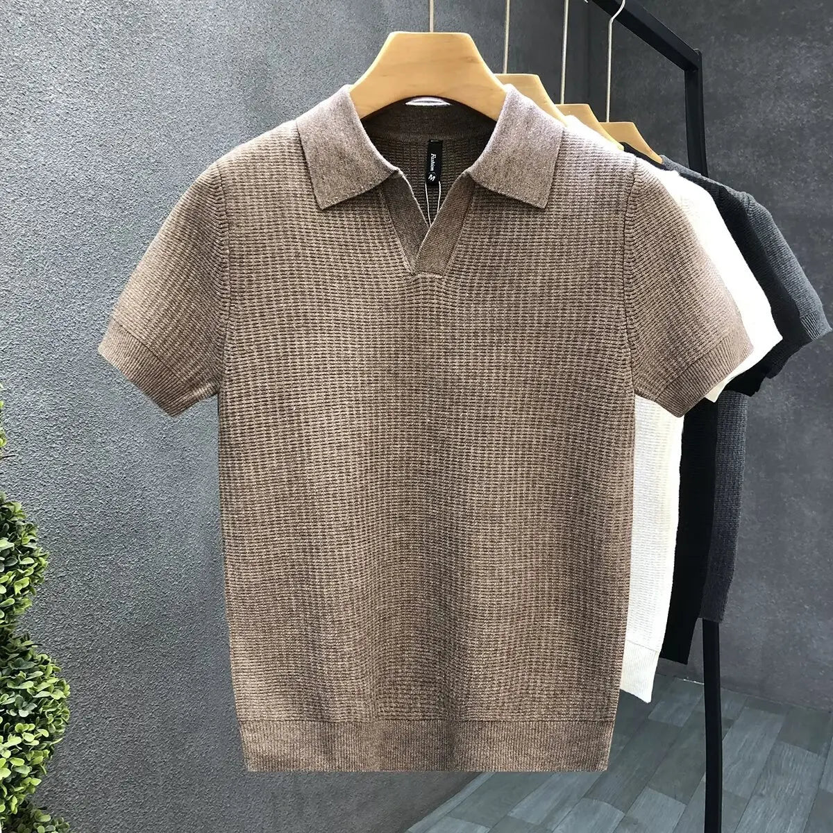 Brown textured polo shirt on a hanger against a gray wall.