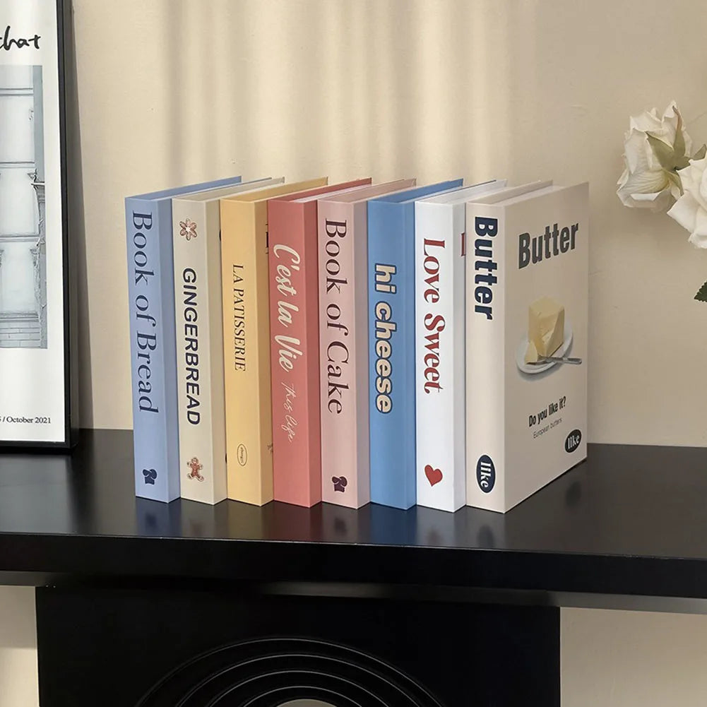 Row of decorative books titled 'Book of Bread', 'Gingerbread', 'La Patissiere', 'C'est la Vie', 'Book of Cake', 'hi cheese', 'Love Sweet', and 'Butter' on a shelf.