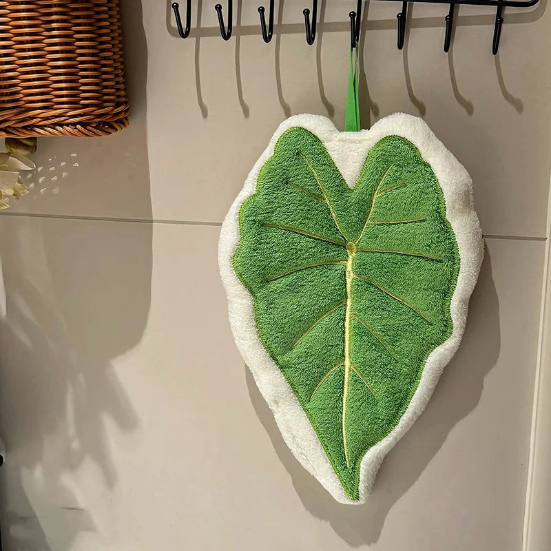 Green leaf-shaped towel hanging on a hook against a tiled wall.