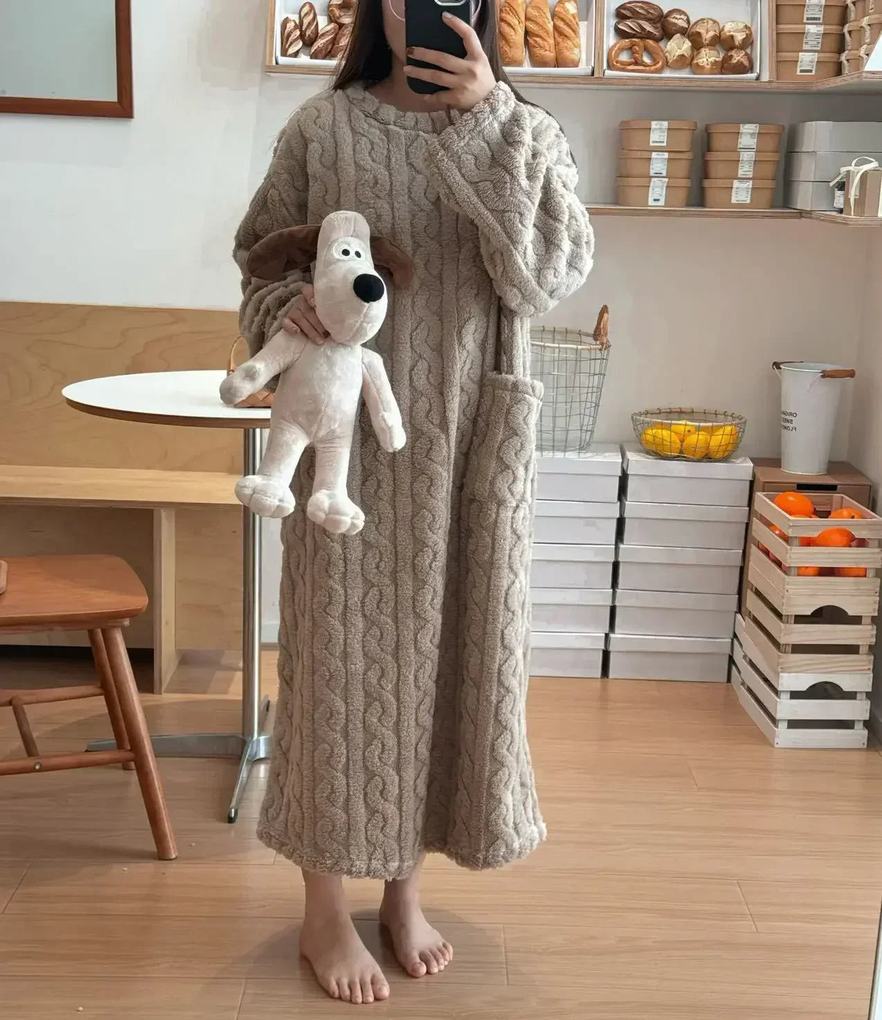 Person wearing a long cable knit robe holding a plush toy in a kitchen.