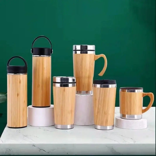 Set of bamboo mugs and tumblers with metal lids on a green background