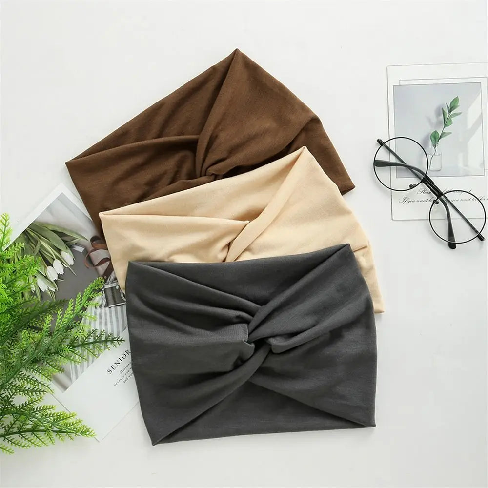 Three headscarves in brown, beige, and gray on a light surface with glasses and a plant.