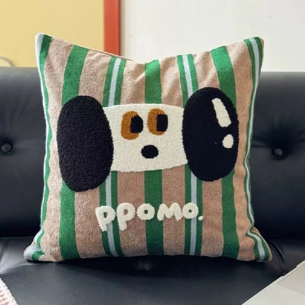 A square throw pillow with a green and beige striped pattern, featuring a raised cartoon dog face with black ears and the text 'ppomo.' in white.