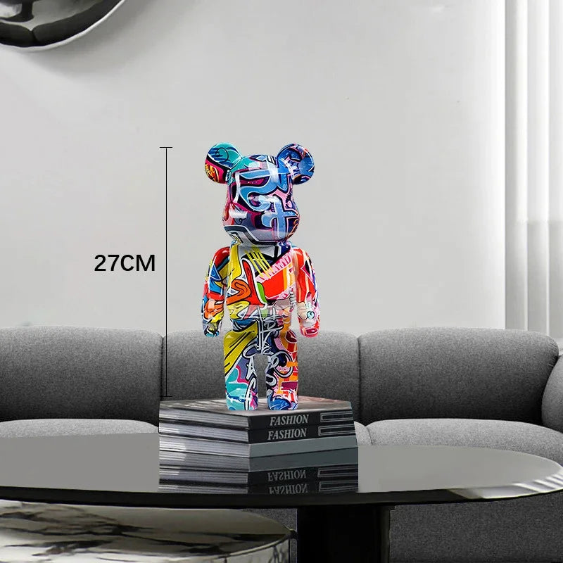 Colorful bear-like figure on a stack of books with a 27cm label, placed on a gray surface.