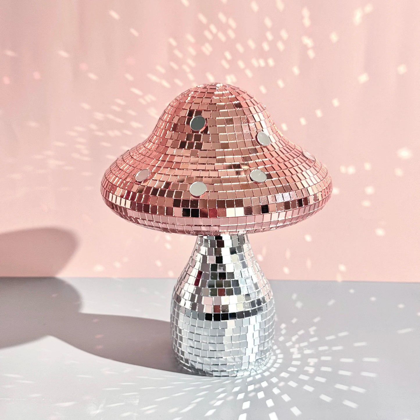Mushroom-shaped ornament with pink top and silver base on a light pink background