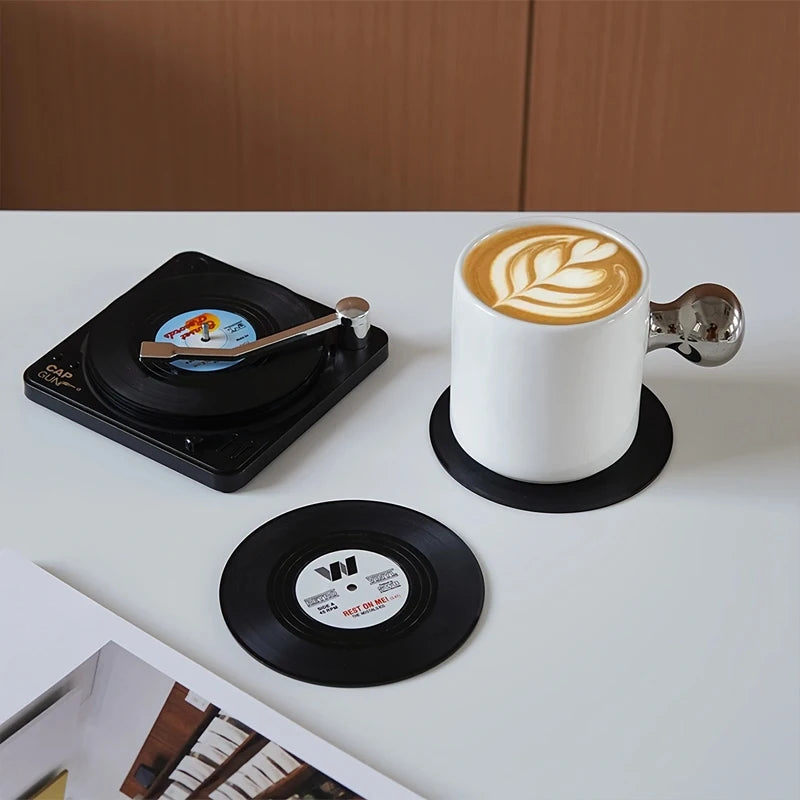 White cup with latte art on a turntable and vinyl record coasters on a white surface.
