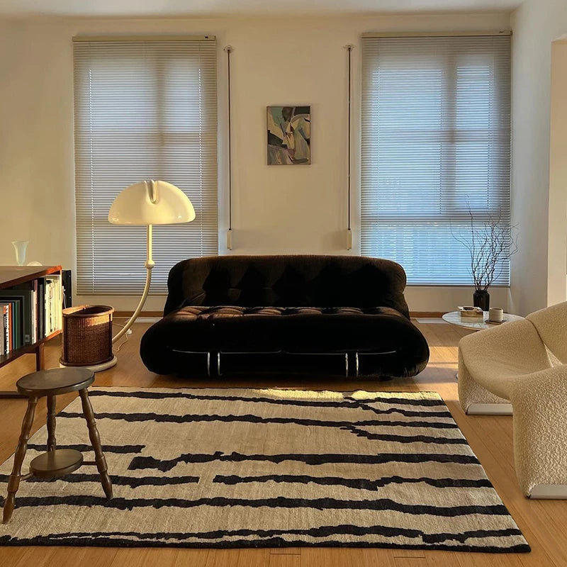 Modern living room with a black sofa, striped rug, and decorative elements.