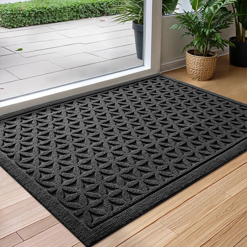 Black doormat with geometric pattern on a wooden floor, leading to a glass door.