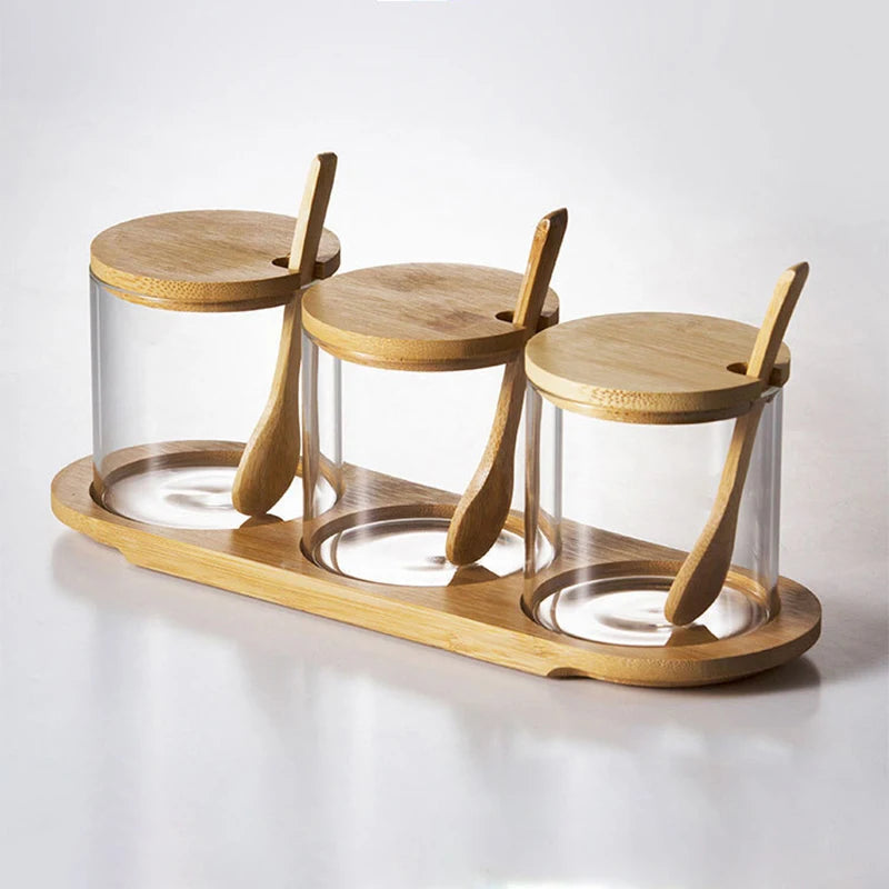 Set of three glass jars with wooden lids and spoons on a wooden tray against a white background
