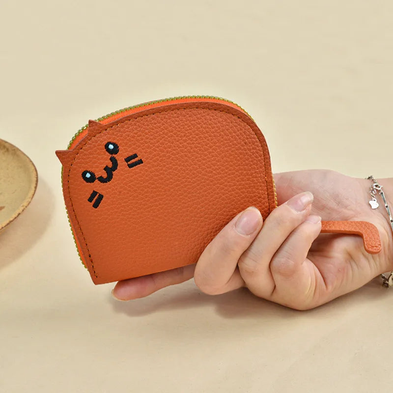 Hand holding a small orange wallet with a cat design on a beige background