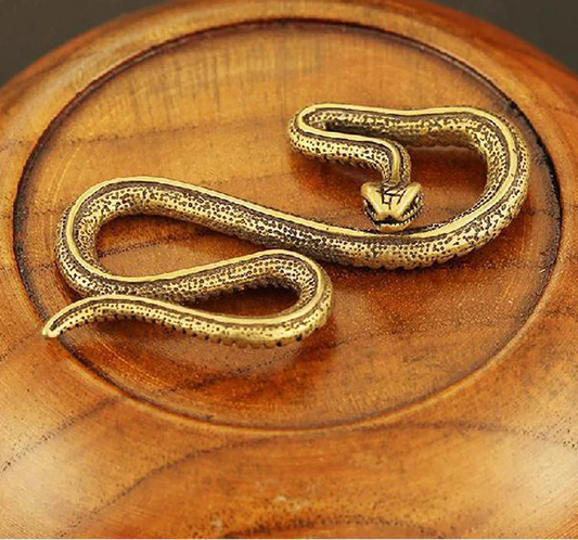 Copper brass mini snake ornament with antique bronze finish on wooden surface