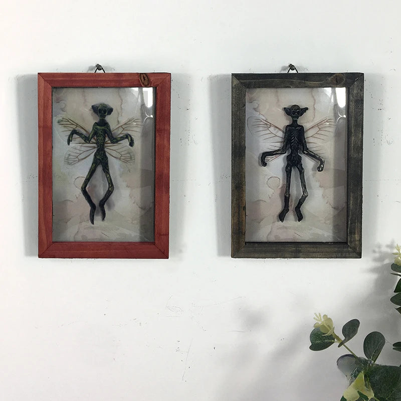 Two framed sculptures of a black figure with wings on a white wall.
