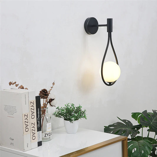 Modern wall lamp with a decorative design on a white wall, next to books and a plant.
