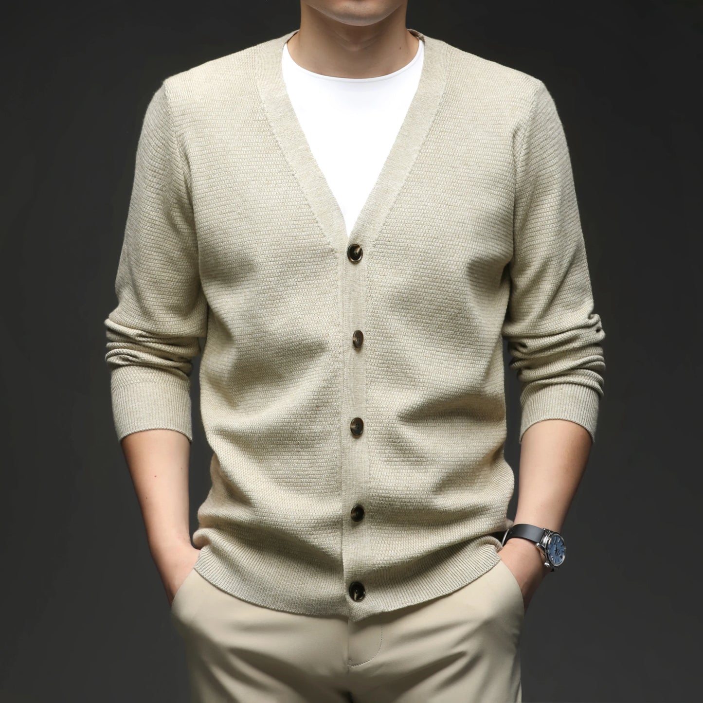 Man wearing a beige cardigan over a white shirt on a dark background