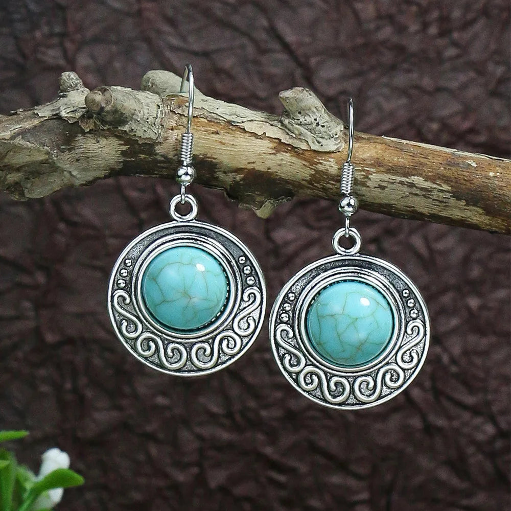 Turquoise earrings with silver circular designs on a wooden branch against a brown background