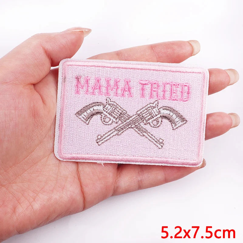 Pink patch with 'MAMA TRIED' text and crossed rifles held in a hand on a white background