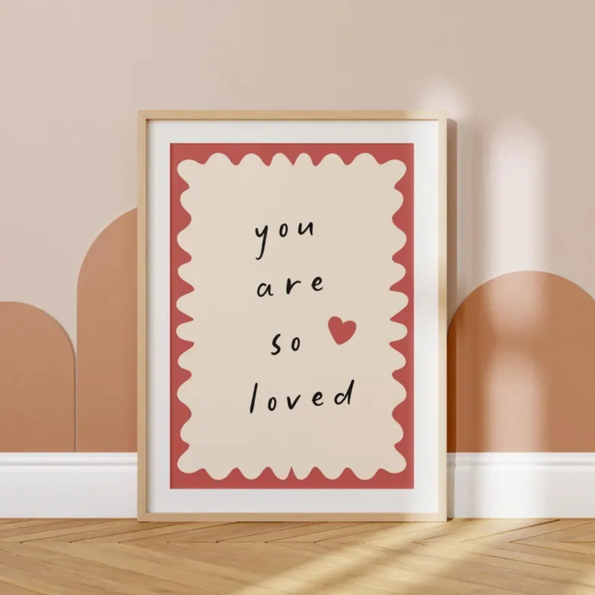 Framed artwork with 'you are so loved' text and heart symbol on a beige wall.