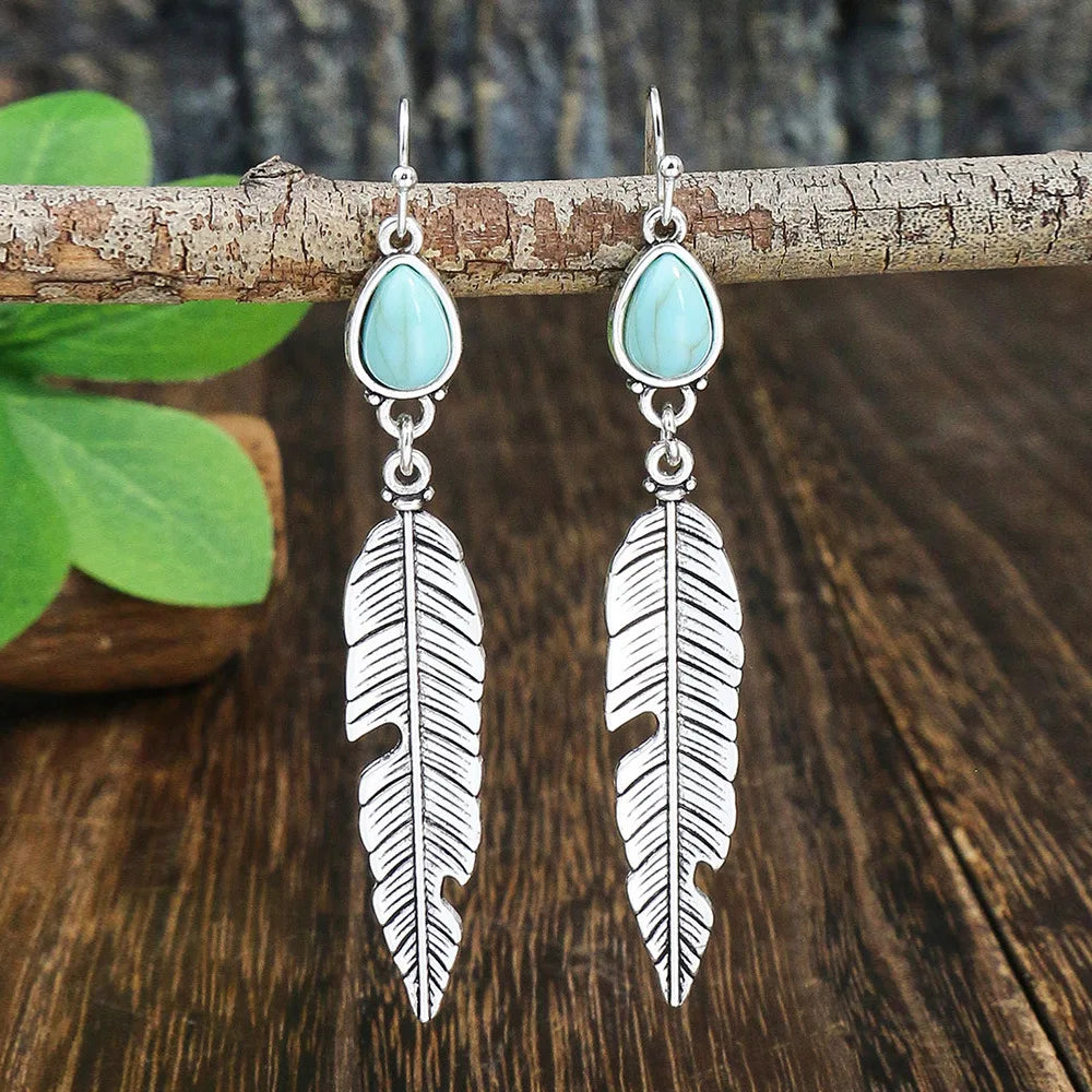 Silver feather earrings with turquoise stones on a wooden branch