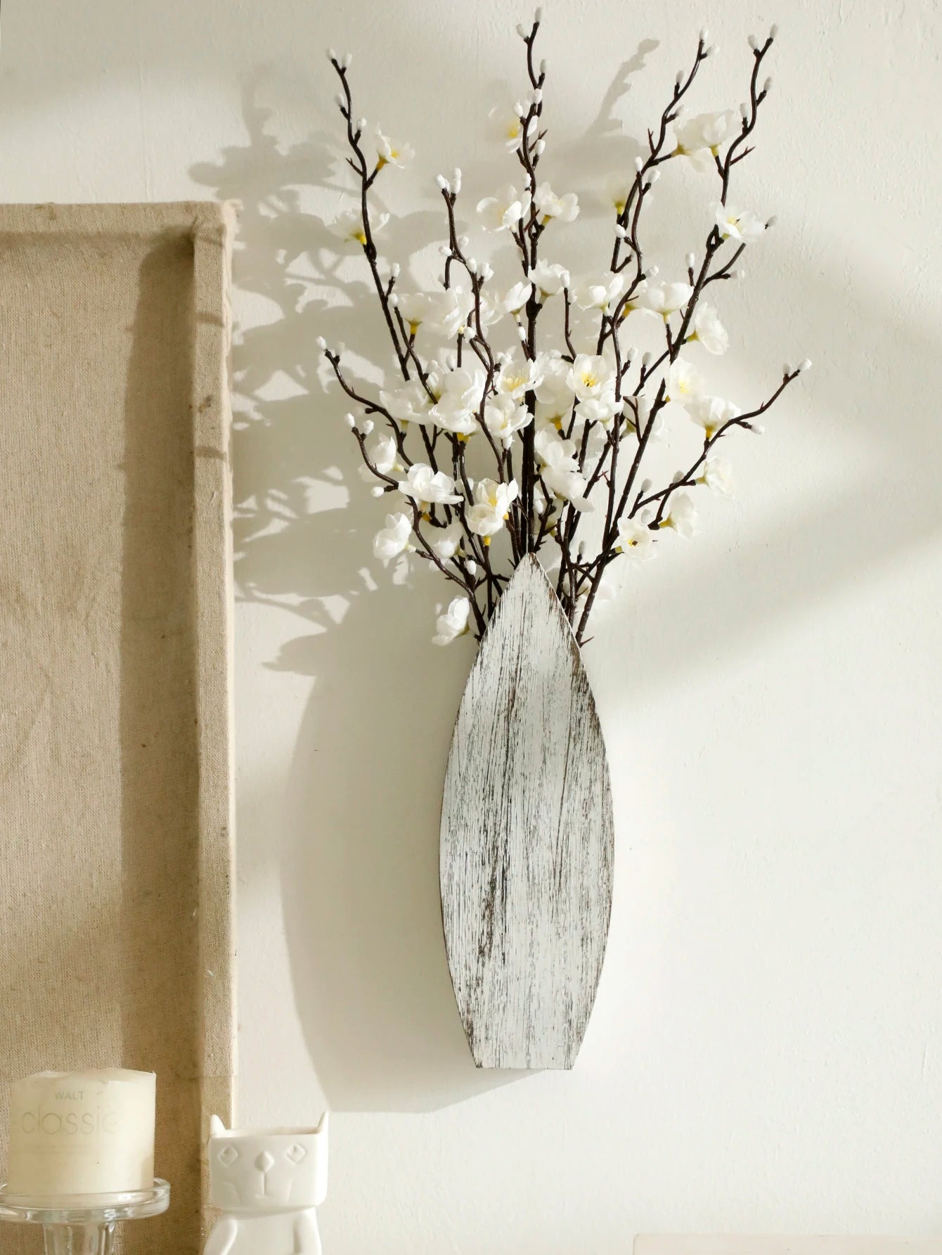 Decorative white surfboard vase with white flowers against a neutral wall