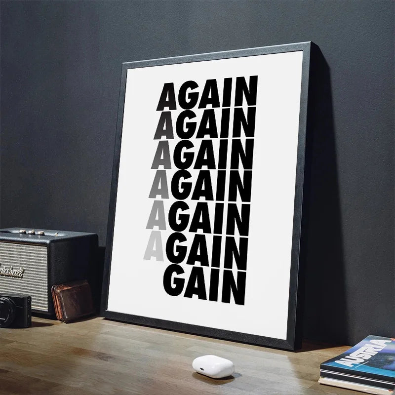 Framed poster with 'AGAIN' text on a white background, placed on a wooden surface with a dark wall.