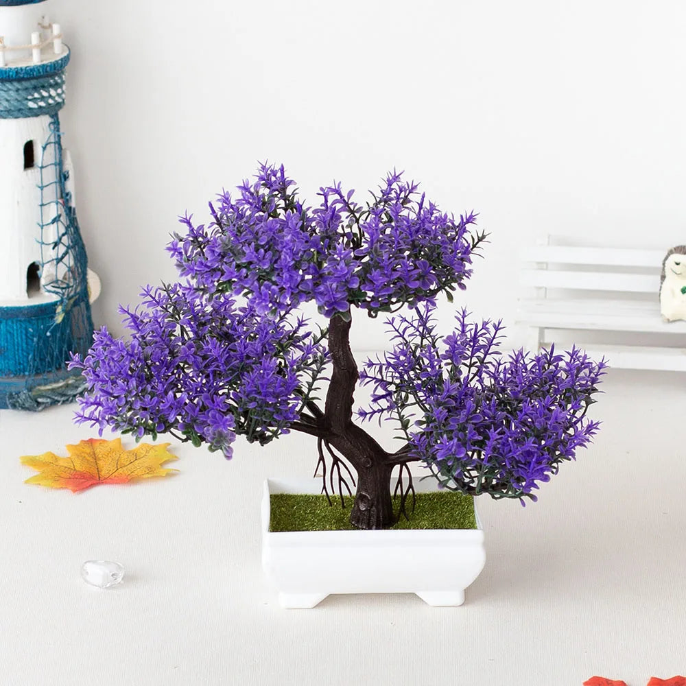 Artificial purple bonsai tree in a white pot on a white surface with decorative elements.