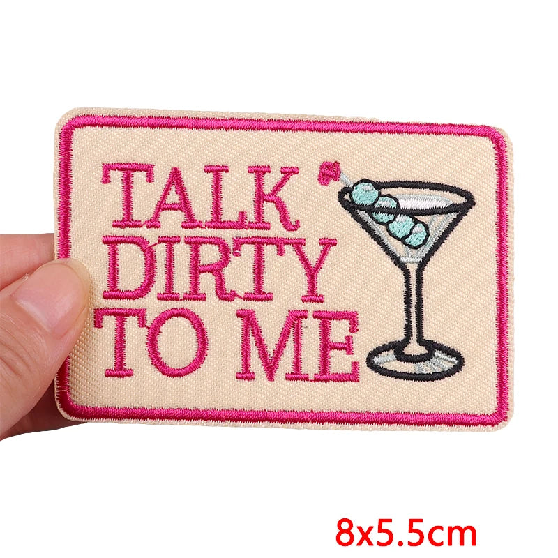 Embroidered patch with 'Talk Dirty to Me' text and a martini glass design, held by a hand.