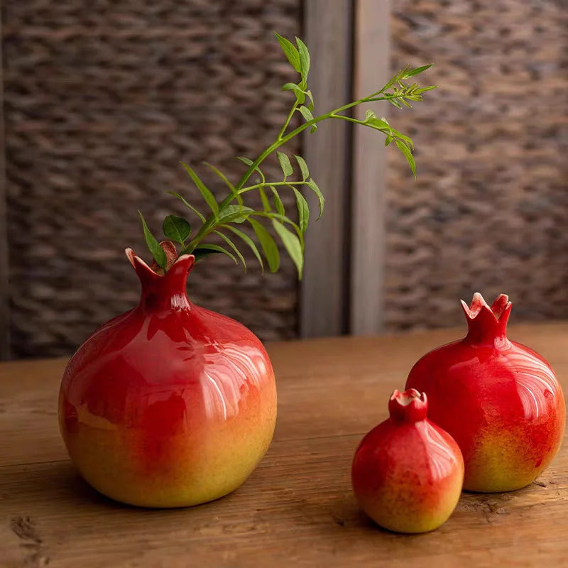 Three red ceramic pomegranate-shaped vases on a wooden surface with a textured wall background.