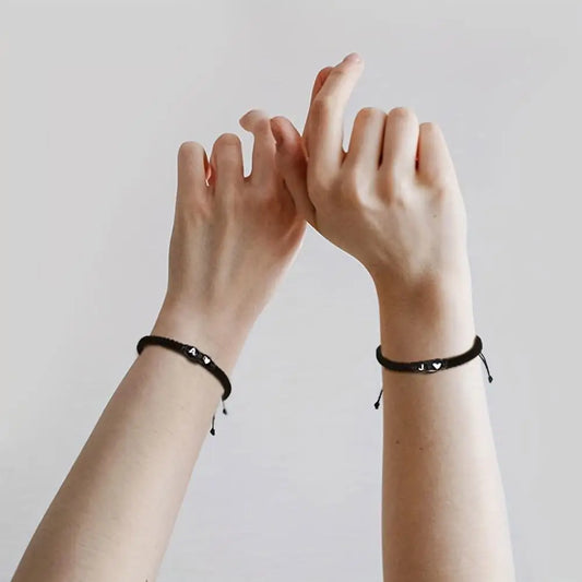 Two hands wearing black bracelets against a plain background