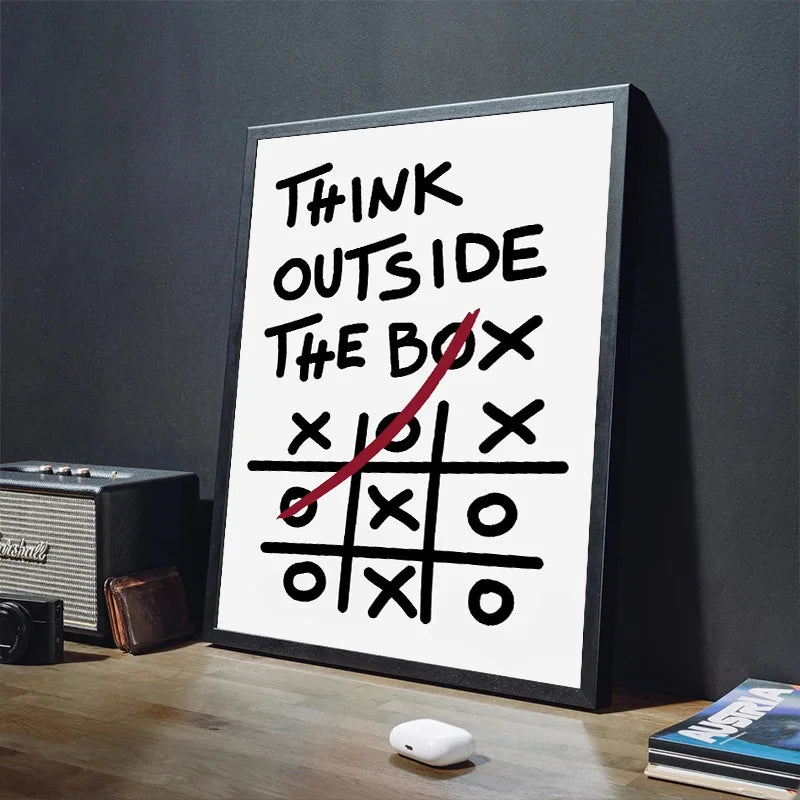 Framed poster with 'Think Outside The Box' and tic-tac-toe on a desk.