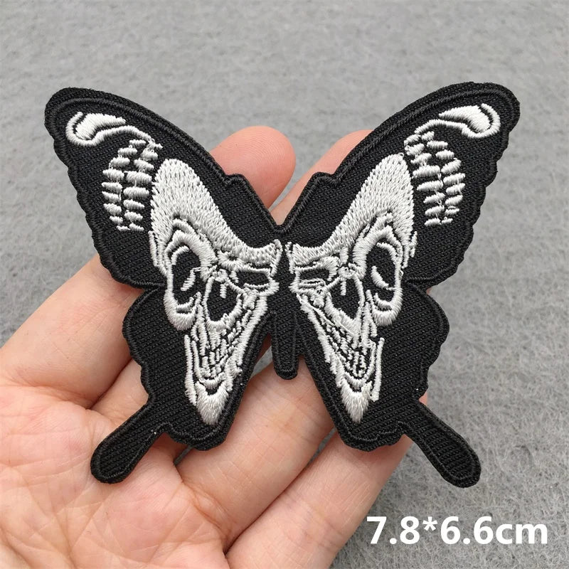 Butterfly-shaped patch with skull design held in hand on gray background