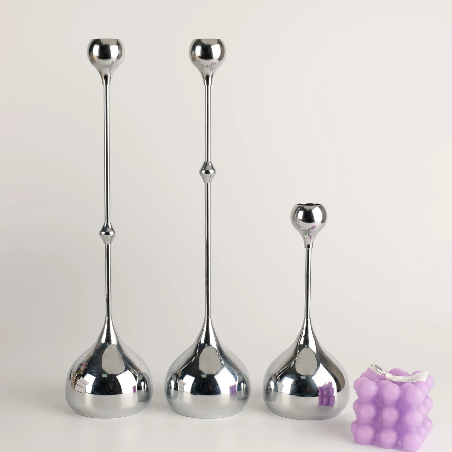 Three silver candle holders of different heights on a white background with a purple candle.