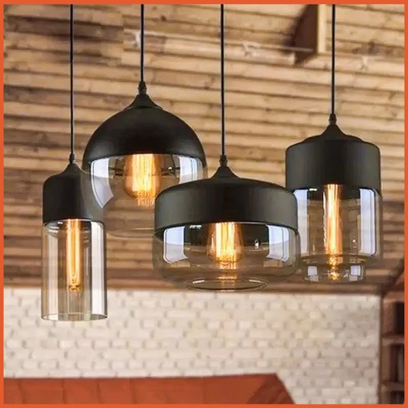 Four pendant lights with black metal and clear glass shades hanging against a wooden wall.