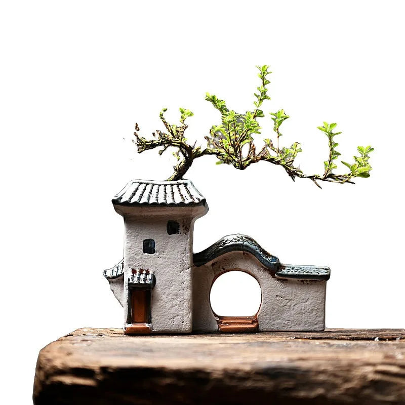 Small miniature house with a bonsai tree on top against a white background