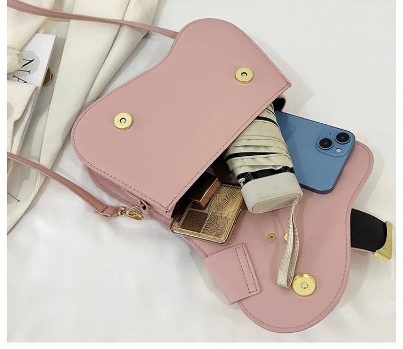 Pink crossbody bag with gold accents containing a phone, wallet, and other items on a white background.