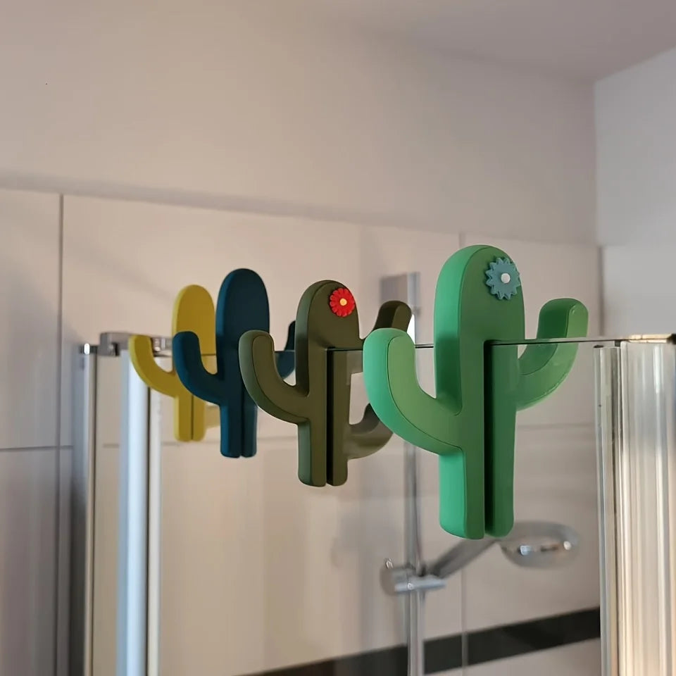 Green cactus shaped bathroom hook hanging over a glass shower door holding towels and accessories