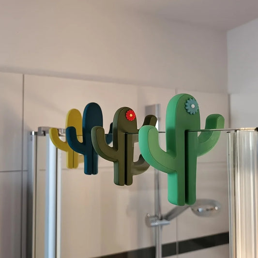 Green cactus shaped bathroom hook hanging over a glass shower door holding towels and accessories