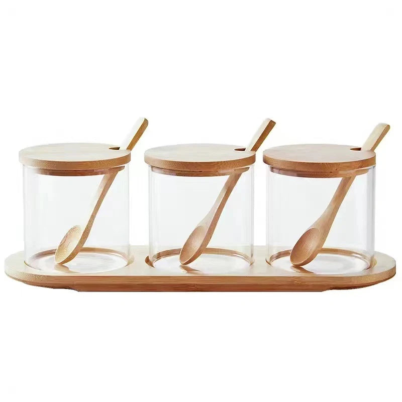 Three glass jars with wooden lids and spoons on a wooden tray against a white background