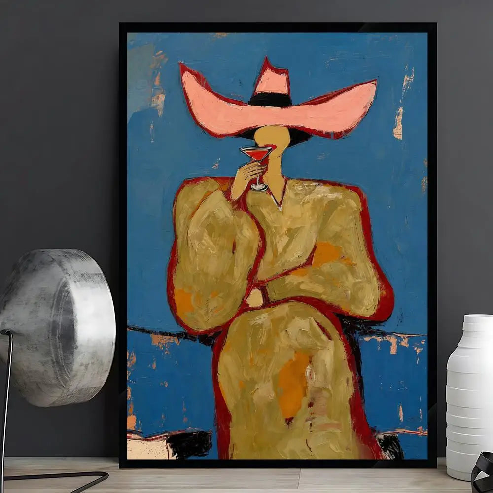A framed abstract art print depicting a stylized figure in a wide pink hat against a textured blue background, displayed on a shelf in a room setting next to a lamp and vase.
