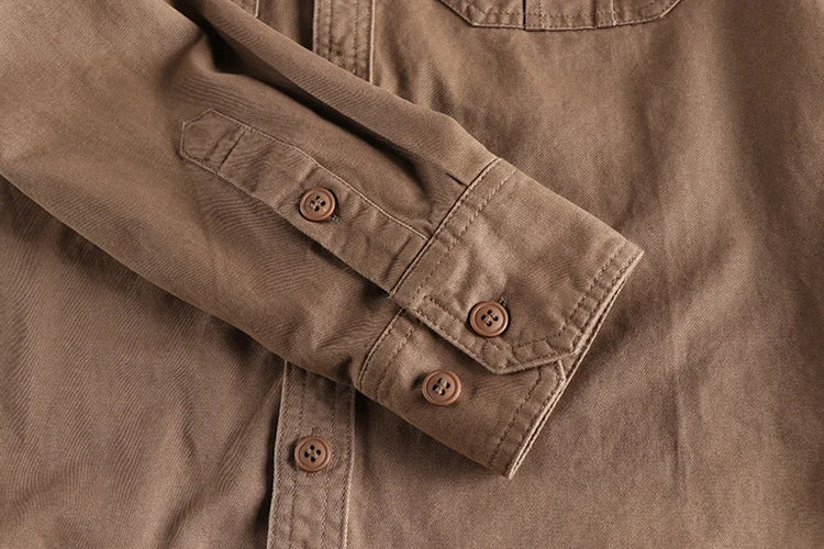Close-up of a brown shirt with rolled-up sleeve and visible buttons.