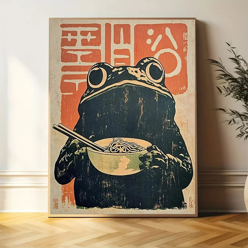 Framed artwork of a frog holding a bowl of ramen with chopsticks, set against a light-colored wall.